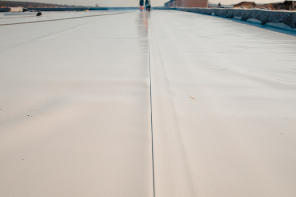 a close-up view of a flat roofing surface showing a smooth white material with a center seam and distant figures walking along it emphasizing a clean roofing project with six key features