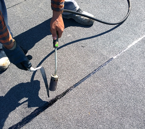 worker applying roofing material using a trowel and torch on flat surface for durable sealing and waterproofing