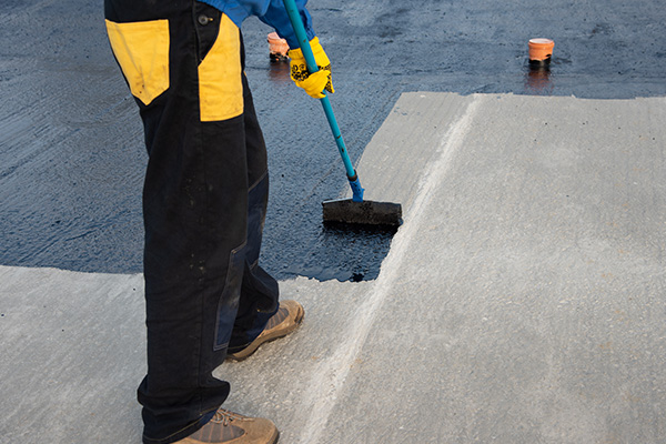 worker applying sealant on concrete surface using roller tools for waterproofing and sealing tasks