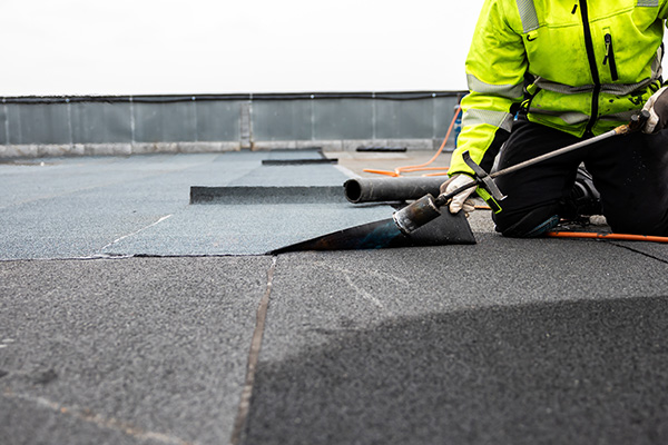 worker installing roofing material on a flat roof using a trowel for a quality finish ensuring durability and safety in construction 6 essential roofing techniques