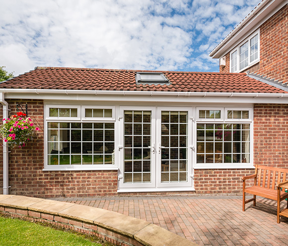 brick house extension with double doors and windows brightened by natural light and surrounded by green lawn and flowers