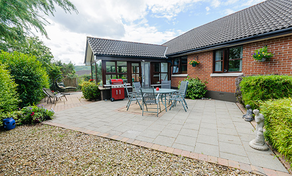 spacious patio area with dining set and grill surrounded by greenery and garden decor showcasing two outdoor chairs and two planters