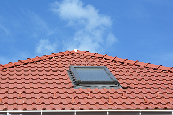 red tiled roof with a skylight against a blue sky showcasing six individual tiles on each row