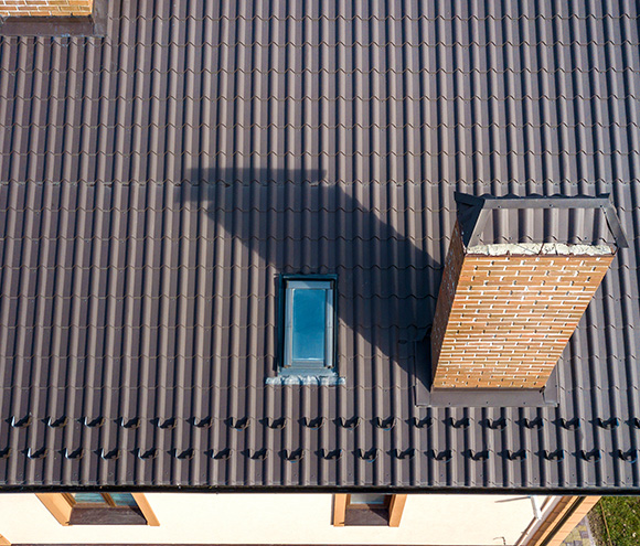 aerial view of a dark metal roof with a small window and a brick chimney showcasing features for durable roofing options and five key benefits of modern roofing systems