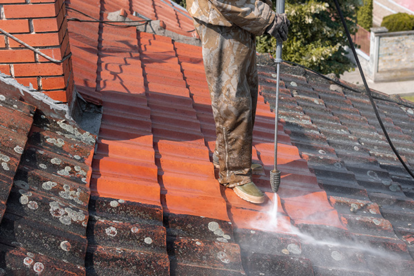 person using a pressure washer to clean a roof covered in moss and dirt engaging in essential maintenance for improved home appearance and longevity 3 tips for roof cleaning
