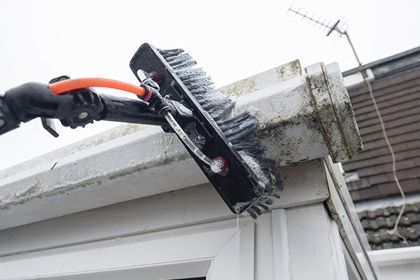 cleaning a roof edge with a brush showing dirt and grime removal tools for effective maintenance