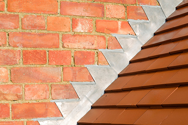 brick wall with metal flashings and brown roof tiles showcasing a three way joint connection for roofing and wall protection