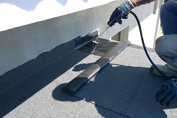person applying waterproofing material on a flat roof using a roller demonstrating effective roof maintenance techniques for protection against water damage and ensuring durability for 8 years