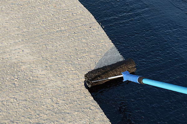 paint roller applying black sealant to a concrete surface representing the number 7 in home improvement projects