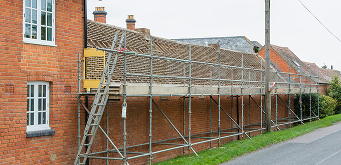 scaffolding along a brick building with a ladder and construction materials on a road near greenery maintenance project seven essentials