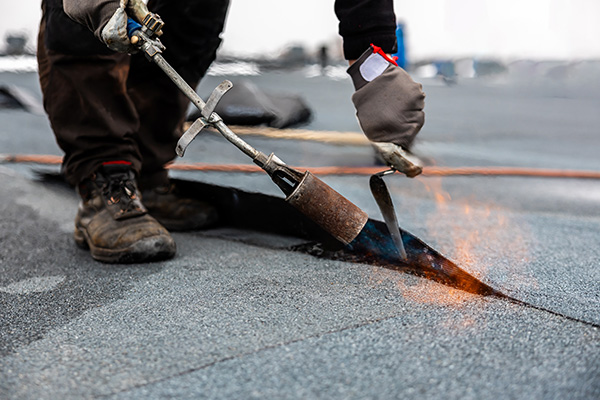 person repairing roofing material using a torch flame in construction site demonstrating roofing techniques and safety