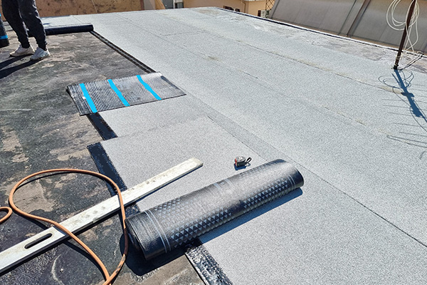 workers installing roofing material on a flat roof with tools and equipment visible durable materials used for roofing 4 different layers