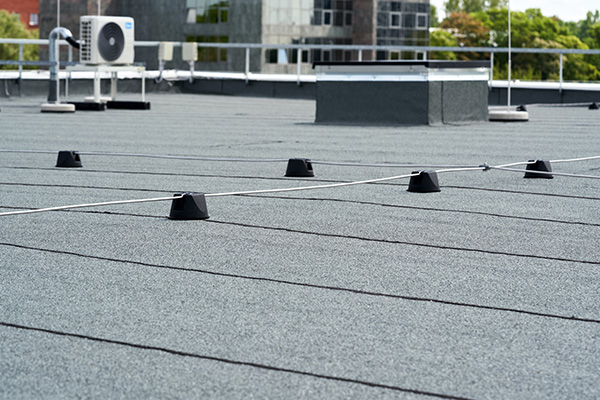 flat roof surface with black rubber membrane showing multiple black cones and a rooftop air conditioning unit in a modern building environment featuring a skyline view over seven distinct elements