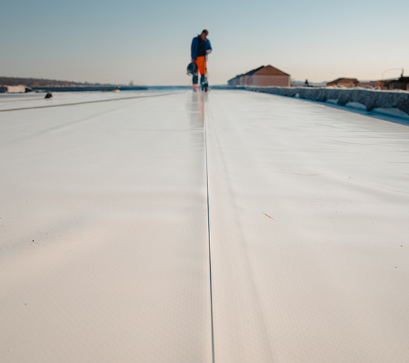 person walking on a wide flat roof under clear sky showing six roofing panels and construction details