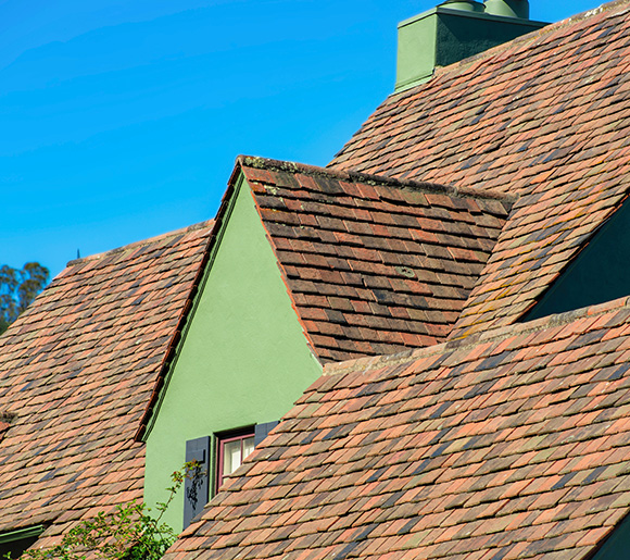 roof of a house with multiple angles and green walls featuring two distinct colors of shingles against a clear blue sky