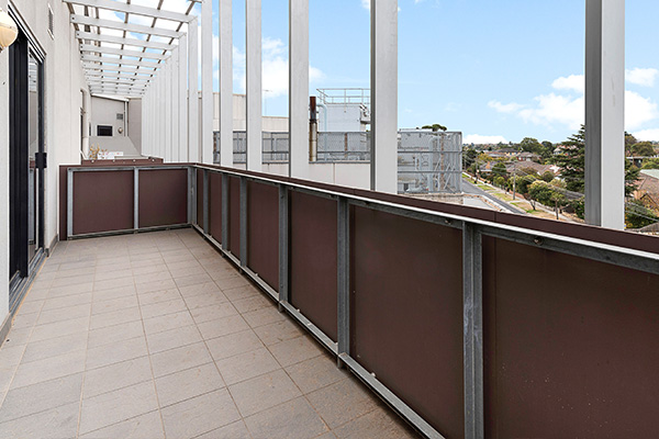 a spacious balcony with white pillars and brown railing overlooking a neighborhood with a blue sky and clouds highlighting the outdoor space and view for two people