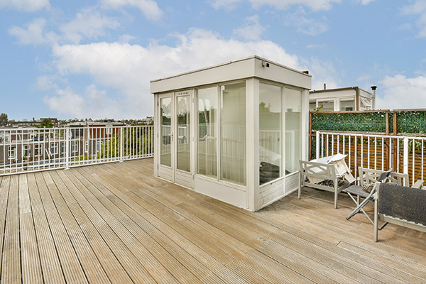 modern glass outdoor room set on a wooden deck surrounded by green foliage featuring six chairs and bright sky