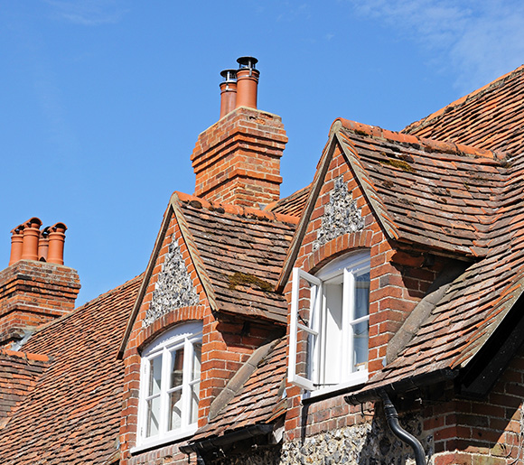 red brick house roof with three chimneys and windows under a clear blue sky