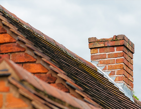 close up of a brick chimney on a sloped roof with red tiles showcasing traditional architecture and home building techniques six roof tiles visible