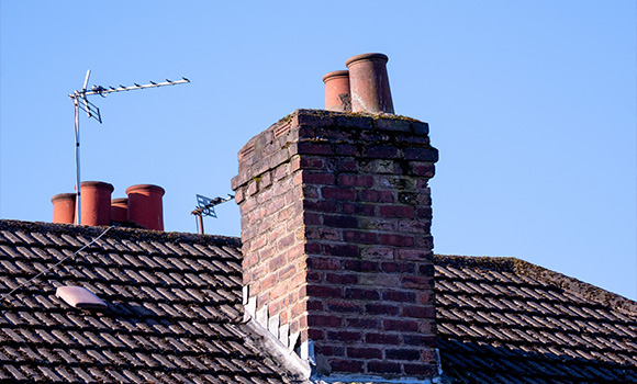 chimney on a rooftop with five chimney pots and an antenna against a clear blue sky