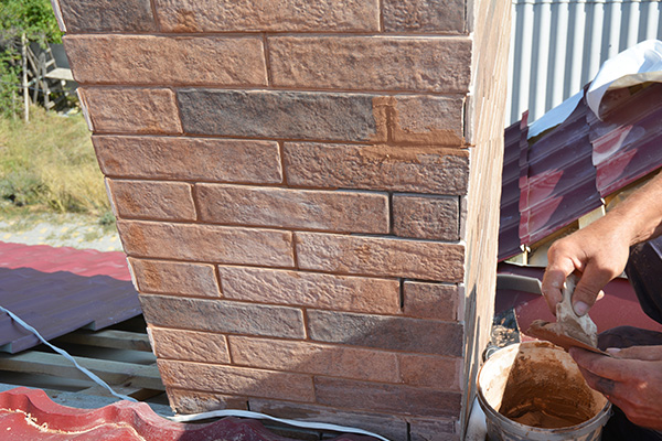 close up of a brick chimney being repaired with hands applying mortar suitable four masonry work and home improvement